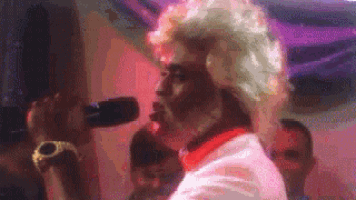 a man in a white wig is singing into a microphone in a club .