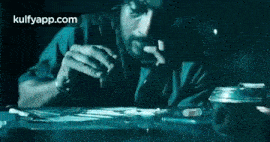 a man is smoking a cigarette while sitting at a table with a cigarette in his mouth .