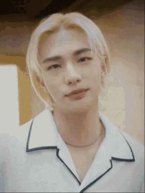 a close up of a man with blonde hair wearing a white shirt and a necklace .