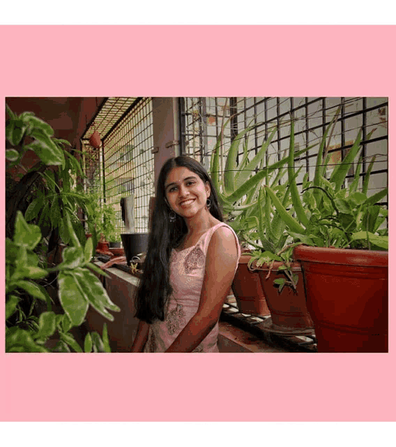 a woman in a pink dress stands in front of potted plants on a balcony