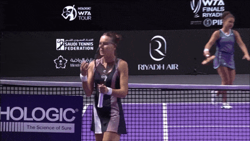 two women playing tennis in front of a riyadh air sign