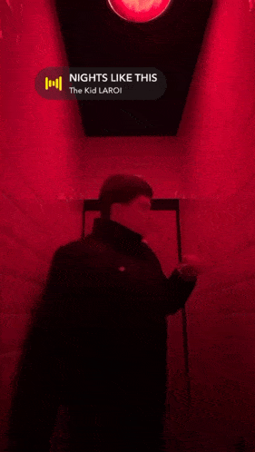 a man leaning against a wall in a hallway with a red light above him that says ' nights like this '