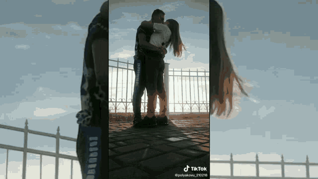 a man and a woman are kissing in front of a fence with tik tok written on the bottom