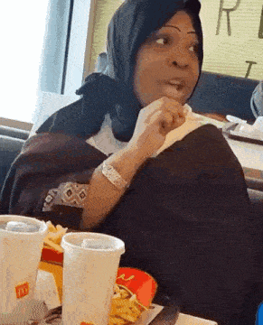 a woman wearing a hijab is sitting at a table in a mcdonald 's eating french fries