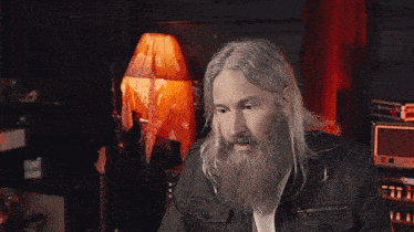 a man with long hair and a beard is sitting in front of a sign that says i 'm just trying
