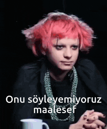 a woman with pink hair and a necklace is sitting in front of a cup .