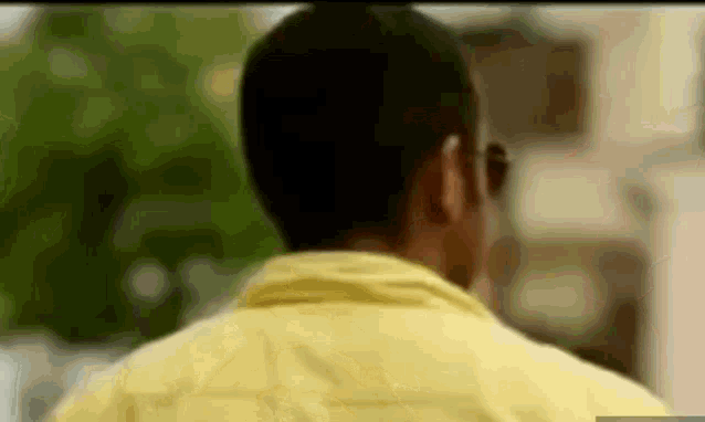 the back of a man wearing a yellow shirt and sunglasses is shown in a blurry photo .