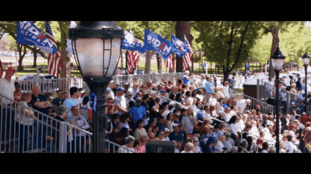 a large crowd of people are gathered in a park with flags that say biden
