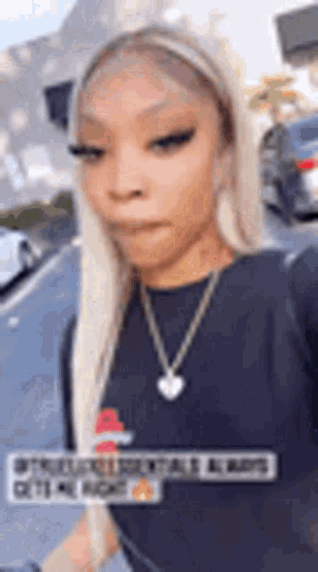 a woman with blonde hair is wearing a black shirt and a necklace while walking down the street .