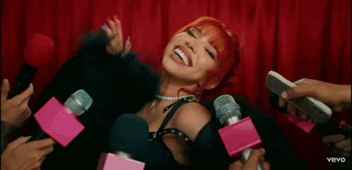 a woman with red hair is surrounded by a bunch of microphones with the word vevo on the bottom
