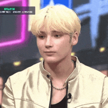 a man with blonde hair is wearing a gold jacket and a black shirt