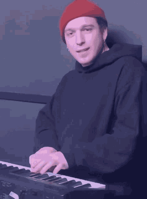 a man wearing a red beanie is playing a keyboard .