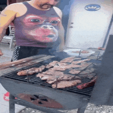 a man in a tank top with a monkey face on it is grilling meat