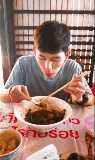 a man is eating a bowl of food with chopsticks .