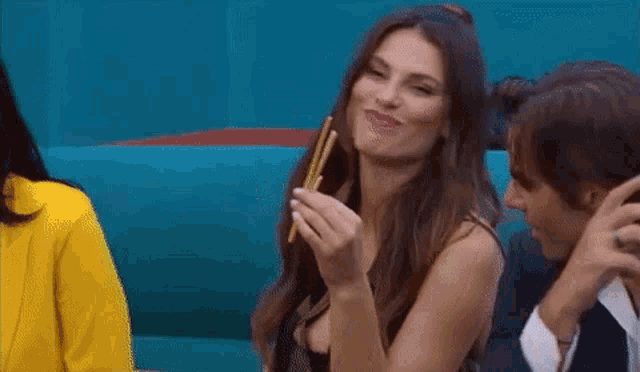 a woman is holding chopsticks in front of her mouth while eating a piece of paper .