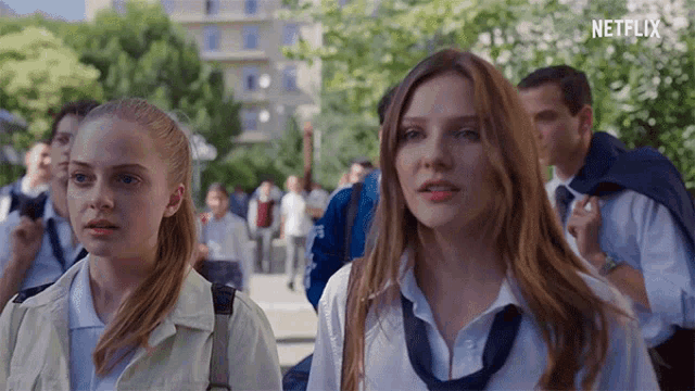 two girls in school uniforms are standing next to each other on a sidewalk .
