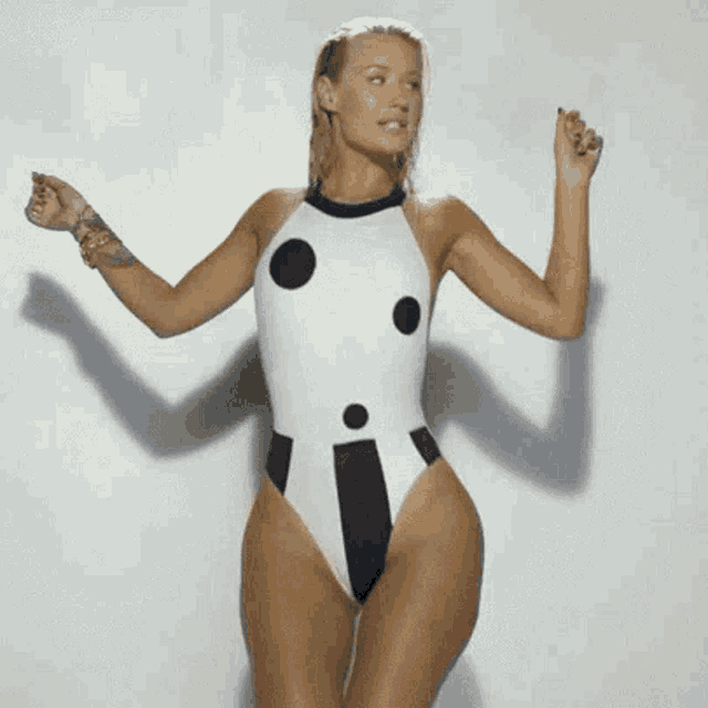 a woman in a black and white polka dot swimsuit is dancing with her arms outstretched .