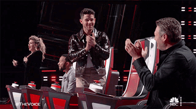 a man in a leather jacket is applauding in front of a group of people on a tv show called the voice