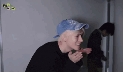 a man wearing a blue hat and a black shirt with the words pow now on it