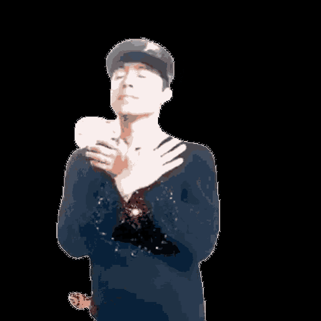 a man wearing a hat and a microphone is holding his hands over his chest .
