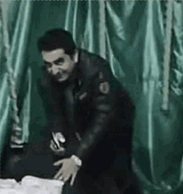 a man in a black jacket is standing in front of a green curtain holding a bottle .