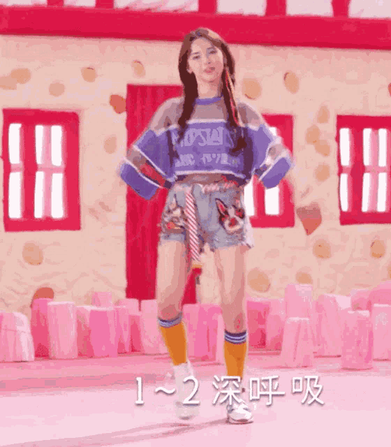 a girl is dancing in front of a pink building with 1-2 written on the bottom right