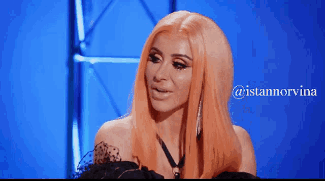 a woman with orange hair is sitting in front of a blue background with the name istannorvina on it