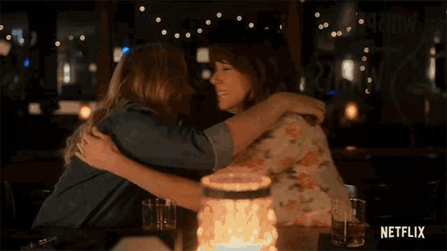 two women hugging at a table with a netflix logo in the corner