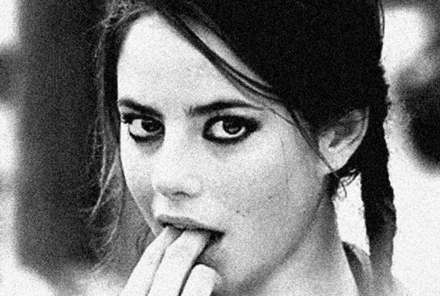 a black and white photo of a woman with pigtails licking her fingers .