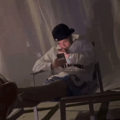 a man wearing a hat and a sweatshirt with the letter c on it looks at his phone
