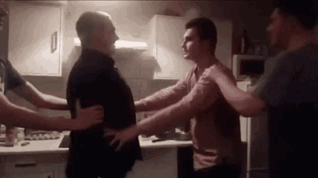 a group of men are standing in a kitchen holding each other .