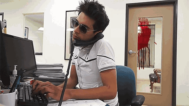 a man wearing sunglasses is talking on a phone while typing on a computer