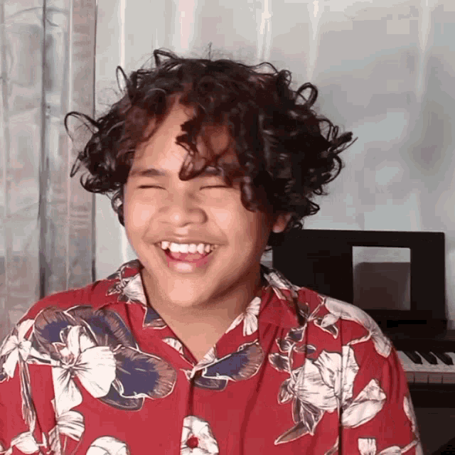a boy with curly hair wearing a red shirt with flowers on it