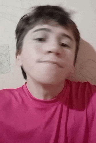 a young boy in a pink shirt is making a face