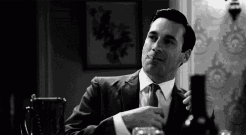 a man in a suit and tie is smoking a cigarette and drinking a glass of wine .