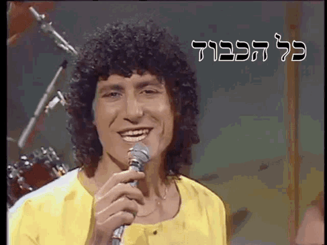 a man with curly hair is singing into a microphone in a yellow shirt .
