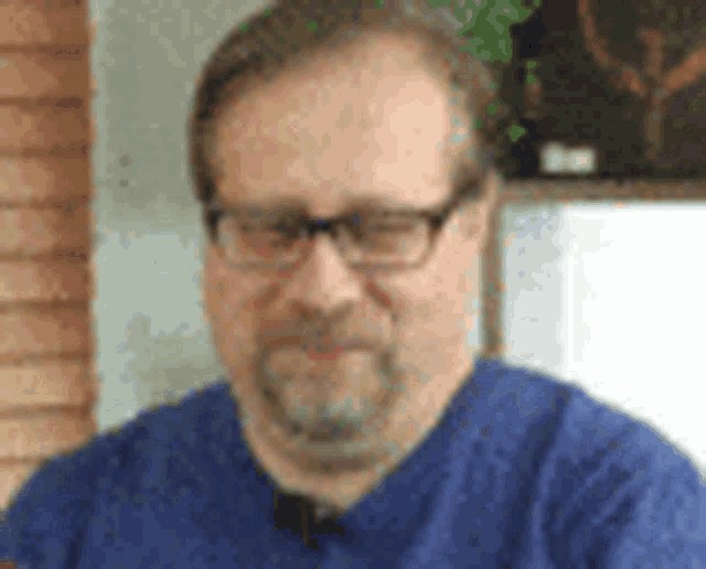 a man with a beard and glasses is wearing a blue shirt and a blue scrub top .