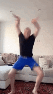 a man in a black shirt and blue shorts is jumping in the air while playing a video game .