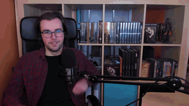 a man sitting in front of a microphone with a bookshelf behind him that has a book called twin peaks