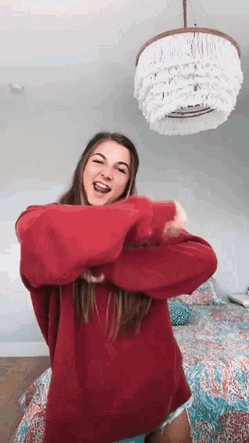 a woman wearing a red sweater is dancing in a bedroom