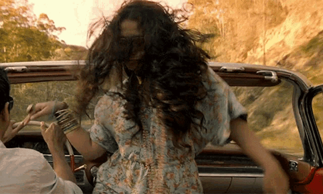 a woman in a floral dress is dancing in a car with her hair blowing in the wind