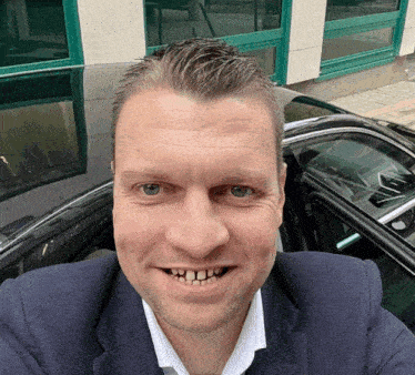 a man in a suit and white shirt is smiling in front of a car
