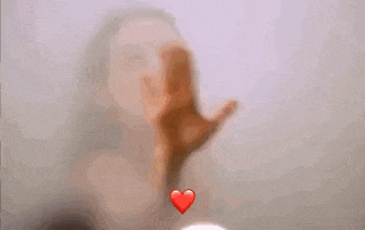 a woman is making a heart with her hands behind a glass .