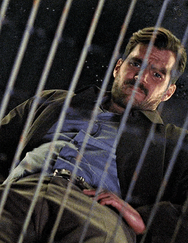 a man with a beard is behind bars and looking at the camera