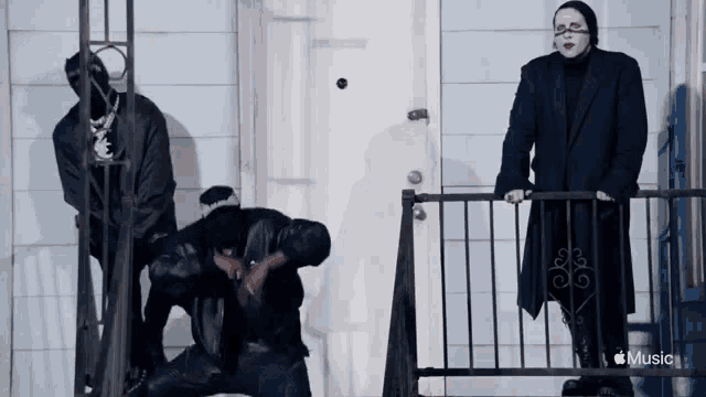 a man in a black suit is kneeling down next to a man in a black suit standing on a balcony .