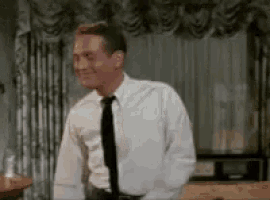 a man in a white shirt and black tie is standing in front of a bed .