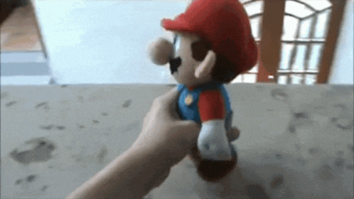 a person is holding a stuffed mario toy on a table
