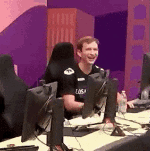 a man is sitting at a desk in front of a computer laughing .
