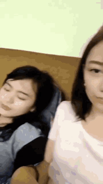 two women are sitting next to each other on a couch and one is sleeping .