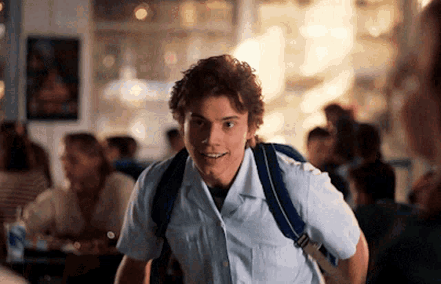a young man wearing a white shirt and a blue backpack smiles